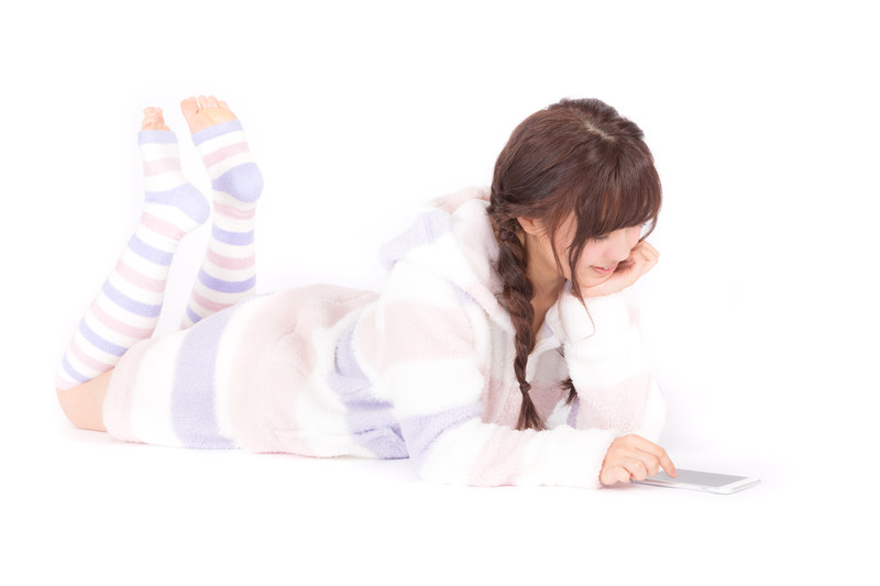 寝転んでスマホを触る女性の画像